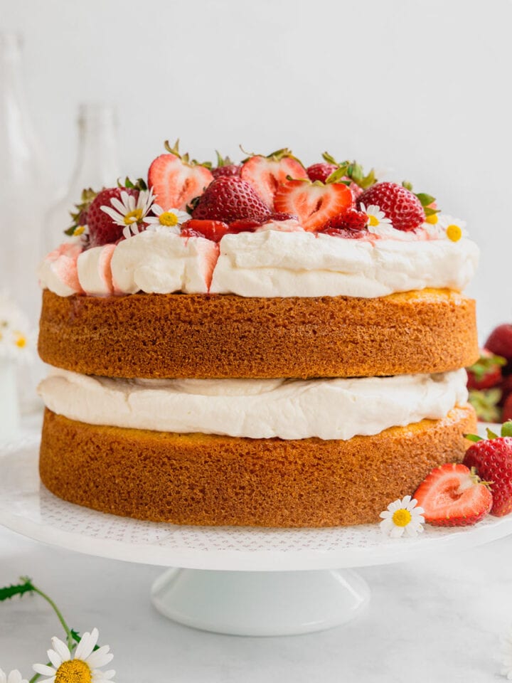 A fresh strawberries and cream layer cake on a white cake stand.
