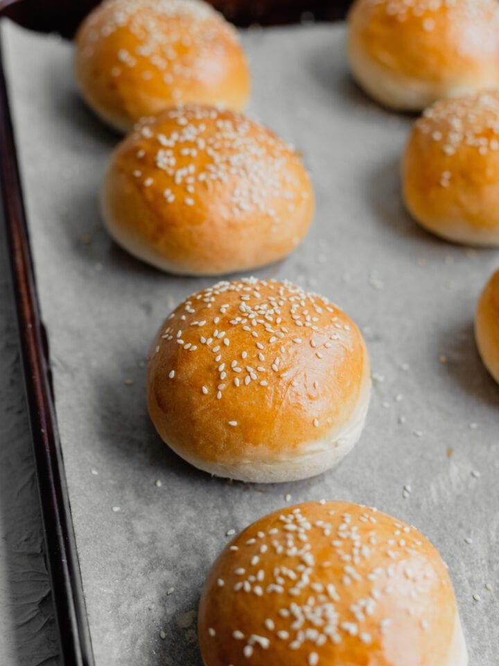 Brioche Burger Buns lined up on a parchment lined baking sheet