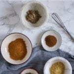 Five different spices are arranged in small bowls on a marble background.