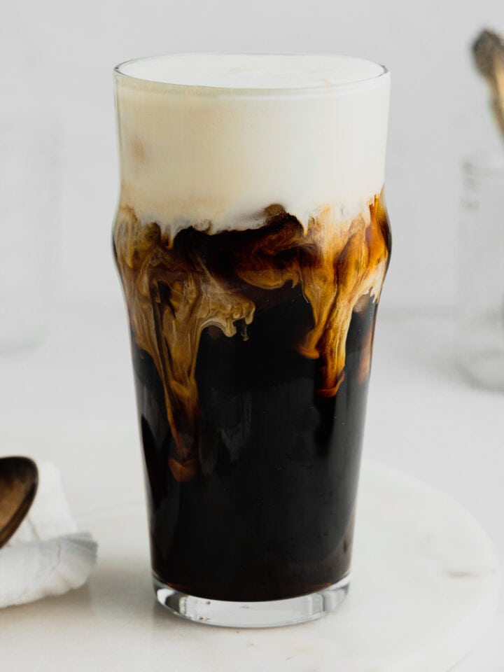 A glass filled with cold brew coffee topped with vanilla sweet cream cold foam sits on a marble serving tray.