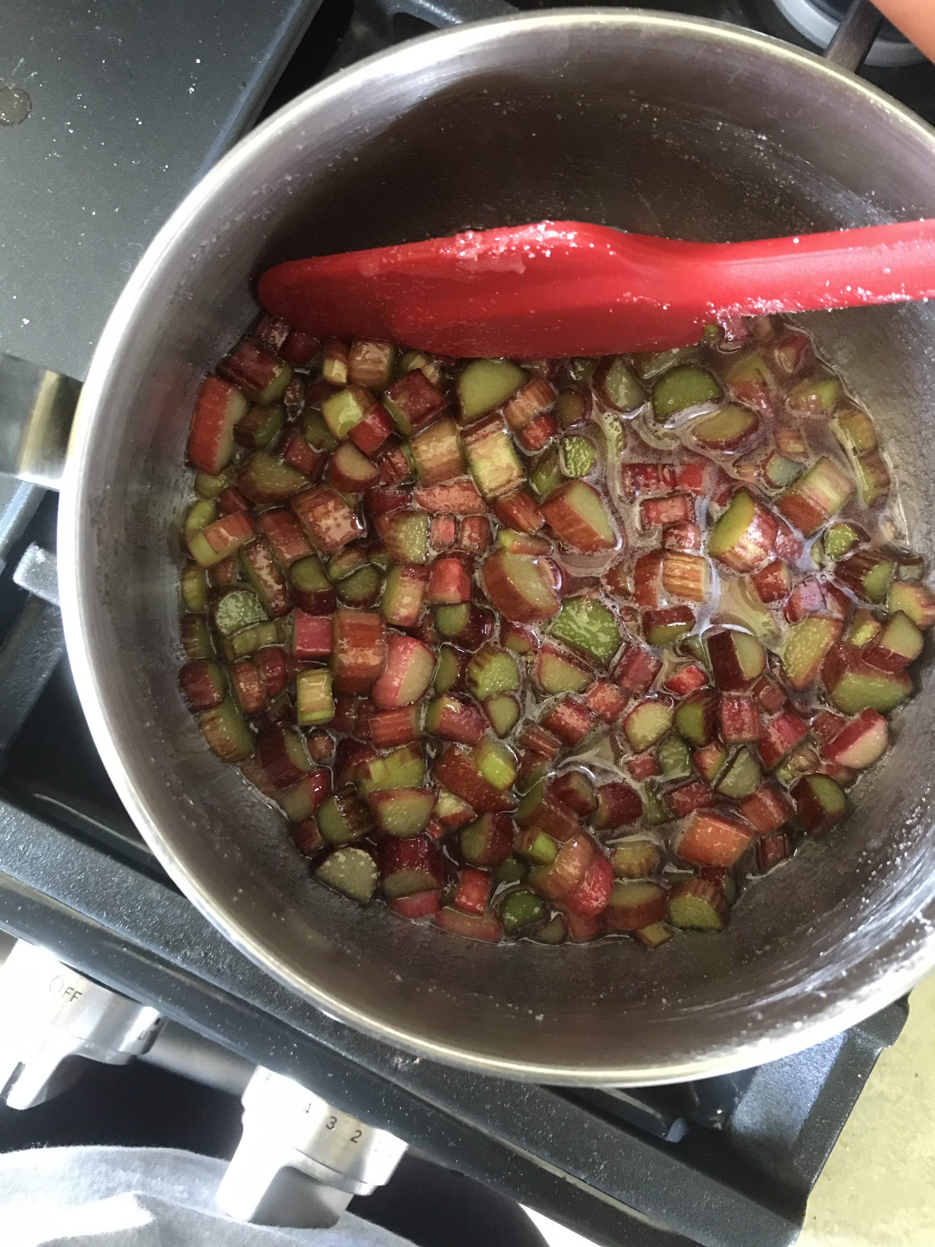 a pot of rhubarb compote sit on a stove. A red spatula is in the pot.