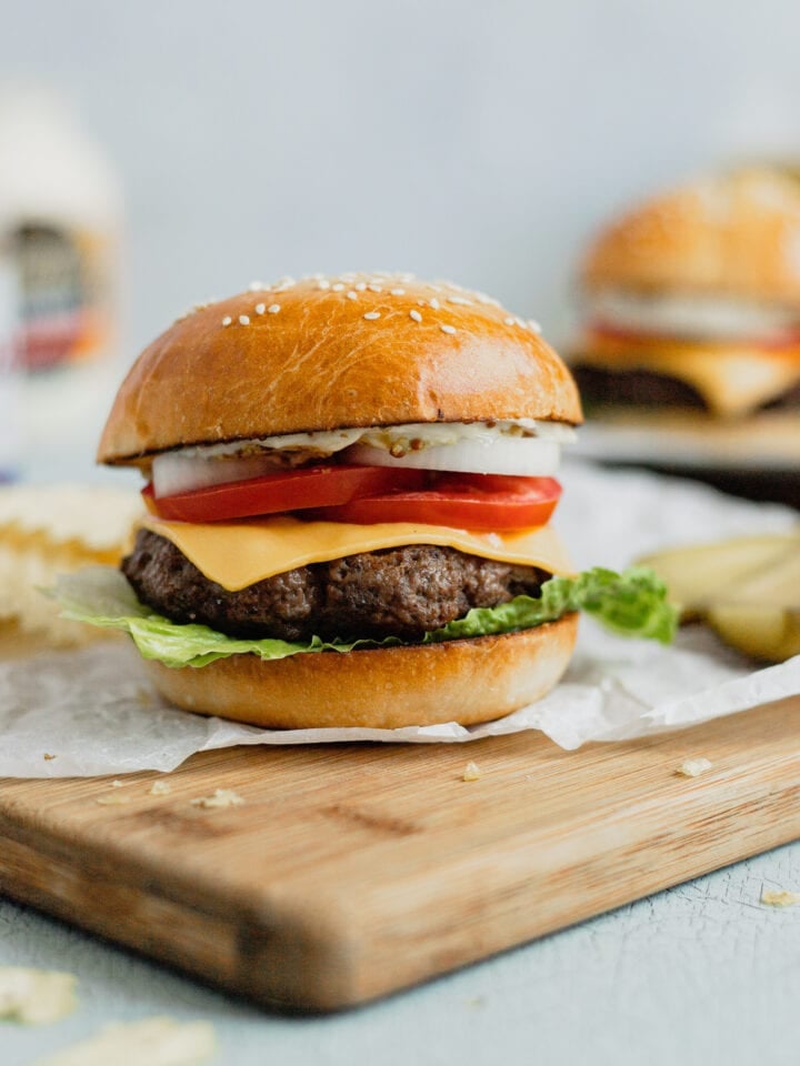 A ground venison burger sits on a cutting board with classic cheeseburger toppings.
