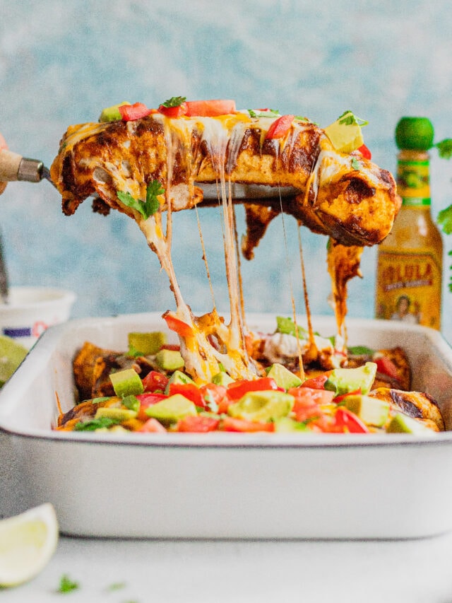 A hand pulls a venison enchilada out of a baking pan and there are strings of cheese being pulled out with it.