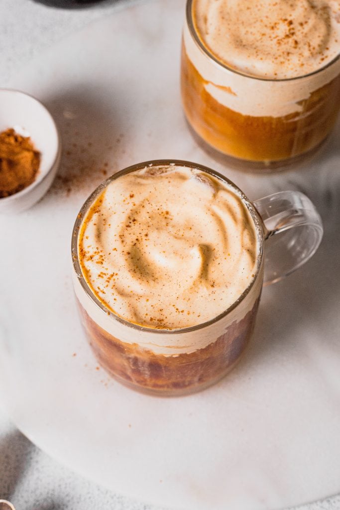 An overhead shot of a homemade glass of pumpkin cream cold foam cold brew coffee on a marble serving board.