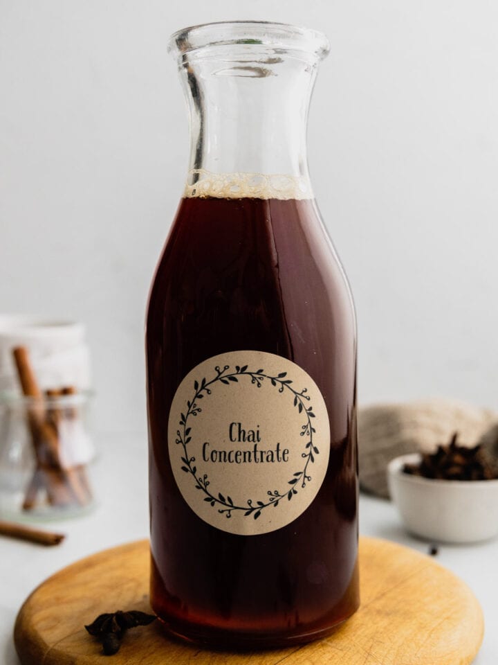 A labeled glass jar is filled with homemade chai concentrate that is dark brown.