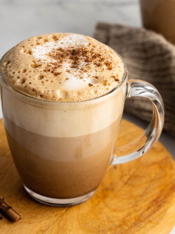 A close up of a clear glass mug filled with a dirty chai latte garnished with chai spice.