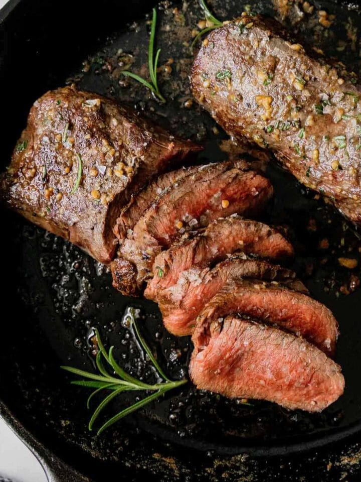 Seared and sliced venison tenderloin in a cast iron pan.