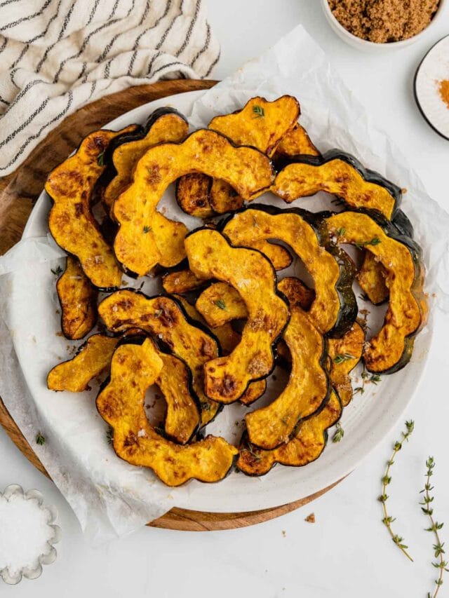 An overhead shot of a white plate filled with slices of air fried acorn squash with a small bowl of brown sugar beside it.