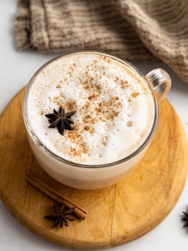 An overhead view of a chai latte on a wooden board garnished with a star anise.