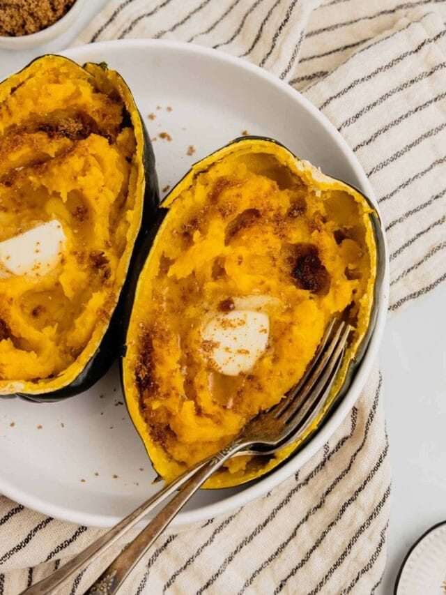 An acorn squash half on a white plate served with butter and brown sugar.