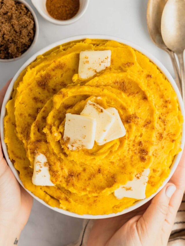 Hands hold a bowl filled with mashed acorn squash topped with butter.
