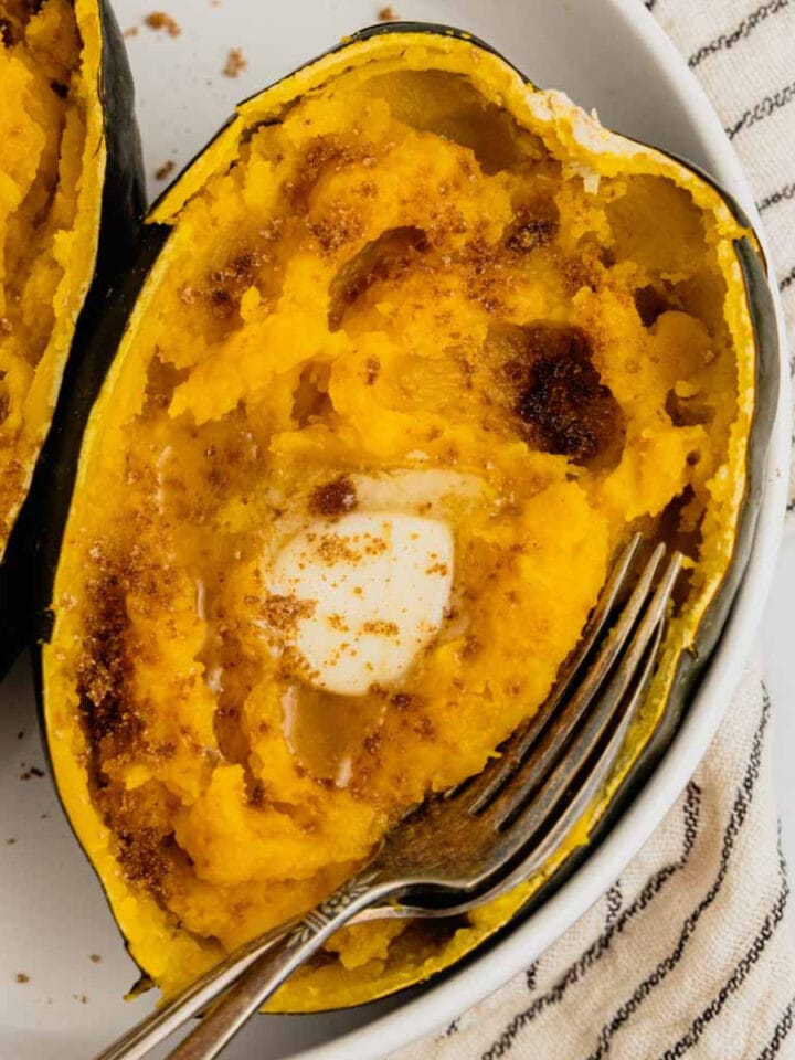 An acorn squash half that's been cooked in the instant pot is on a white plate topped with butter and brown sugar.