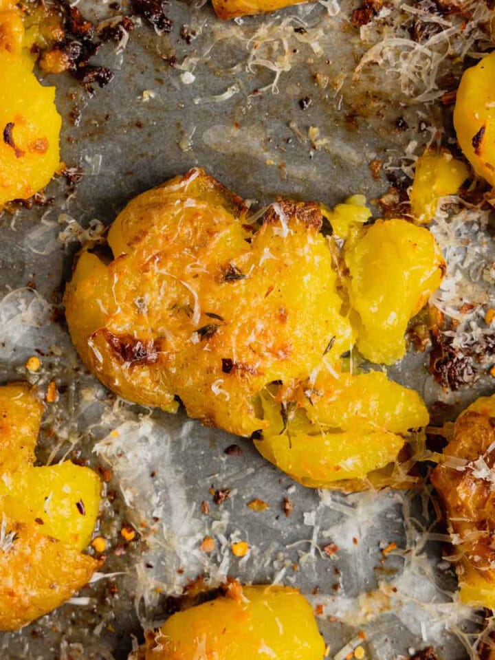 A close up of crispy smashed potatoes topped with shredded parmesan cheese on a rimmed baking sheet.