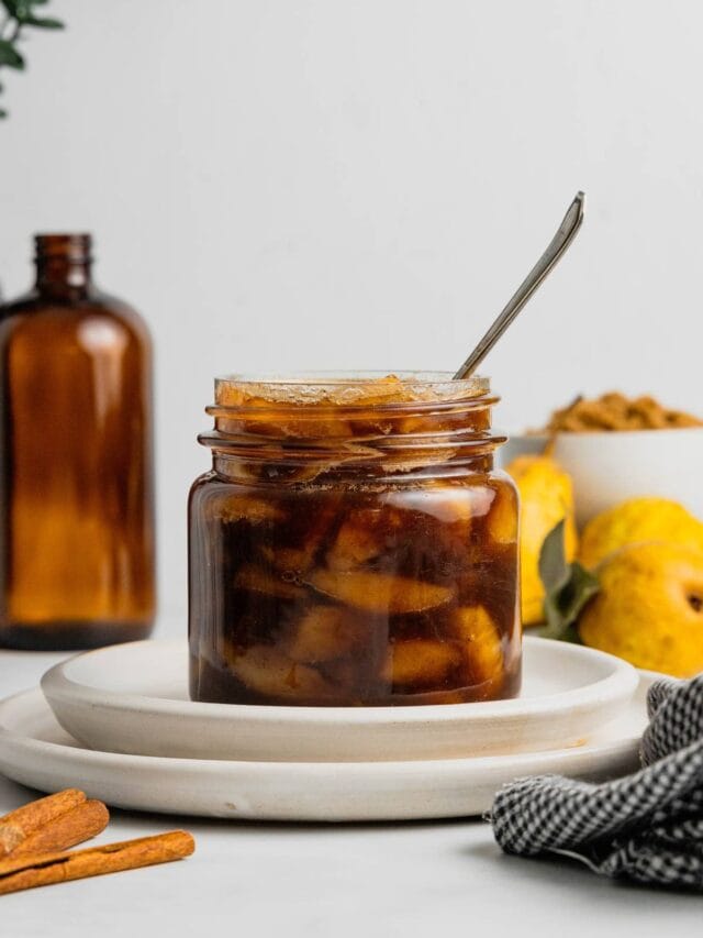A glass jar full of pear compote with a spoon in it on a plate.