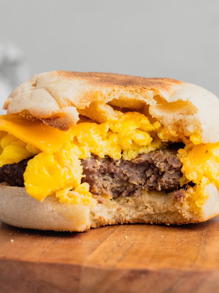 A venison breakfast sandwich with a bite taken out of it on a wooden plate.