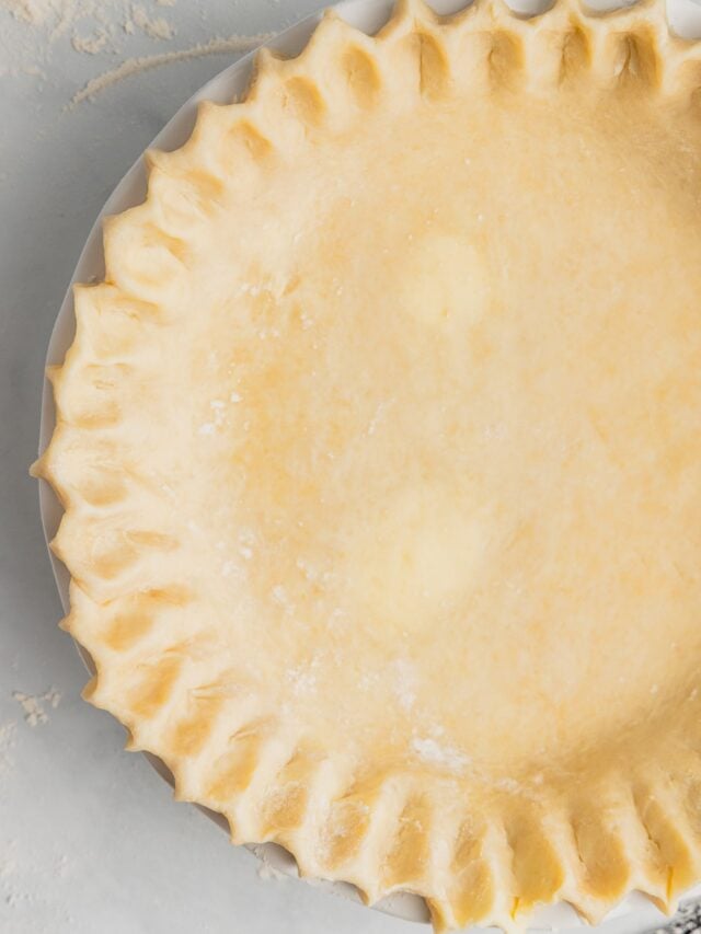 A close up of a pie crust crimped and ready in a pie plate.