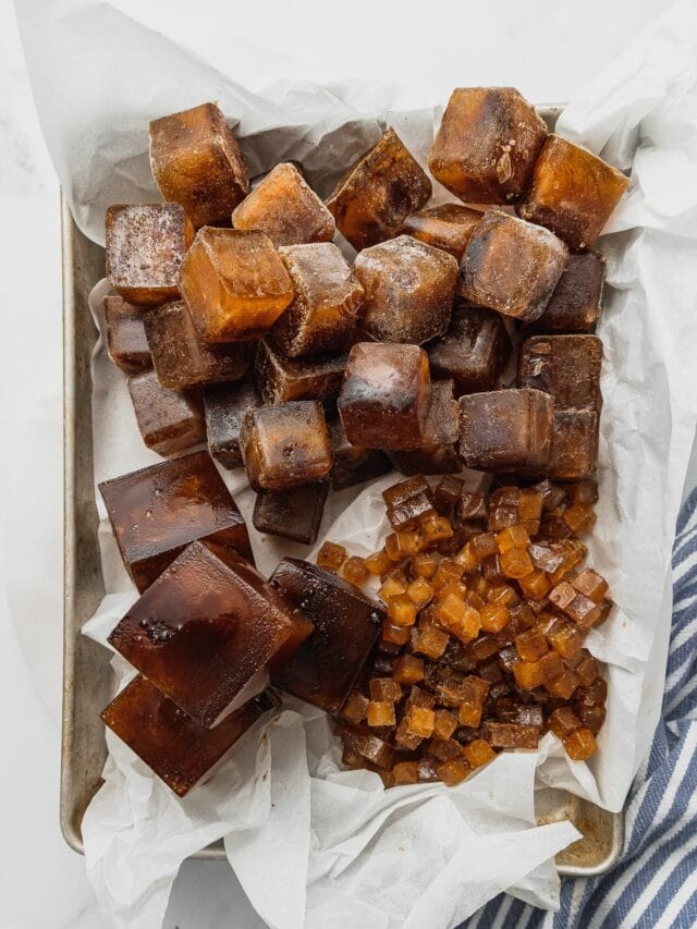 A tray lined with parchment paper holds a variety of different sized coffee ice cubes.