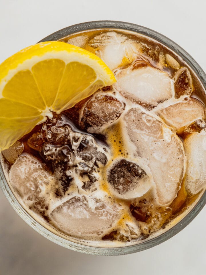 An overhead view of a glass filled with ice, espresso, and tonic water garnished with a lemon wedge.