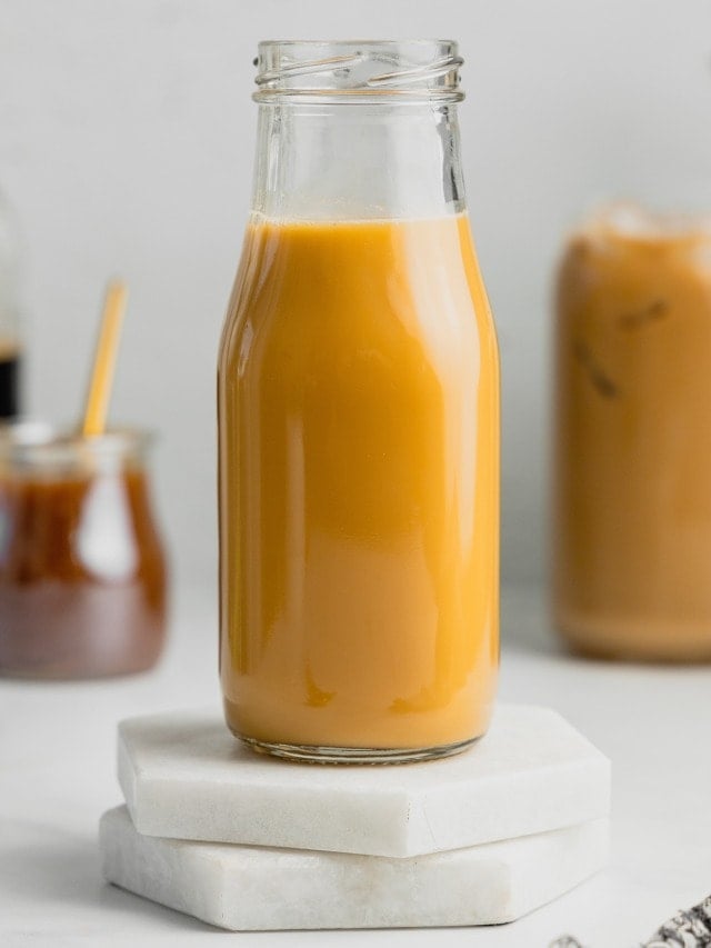 A glass jar filled with caramel simple syrup sits on two white marble coasters.