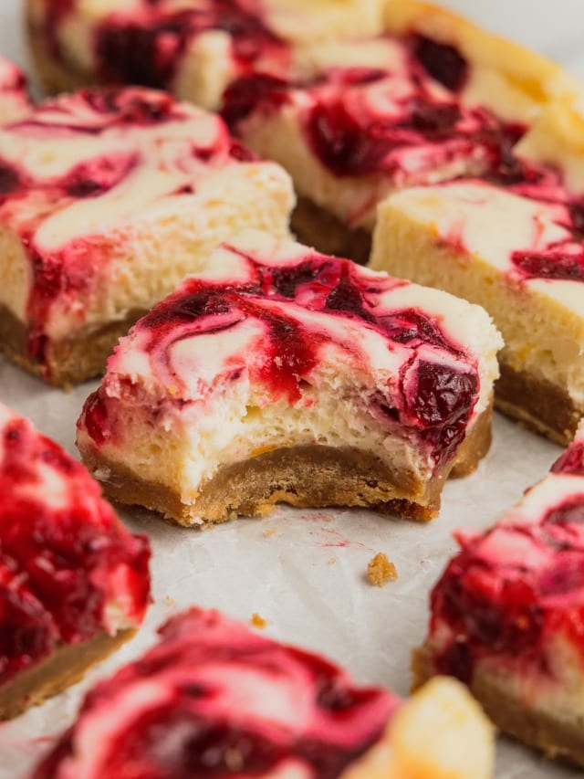 A cranberry cheesecake square with a bite taken out of it sits on a piece of parchment paper.
