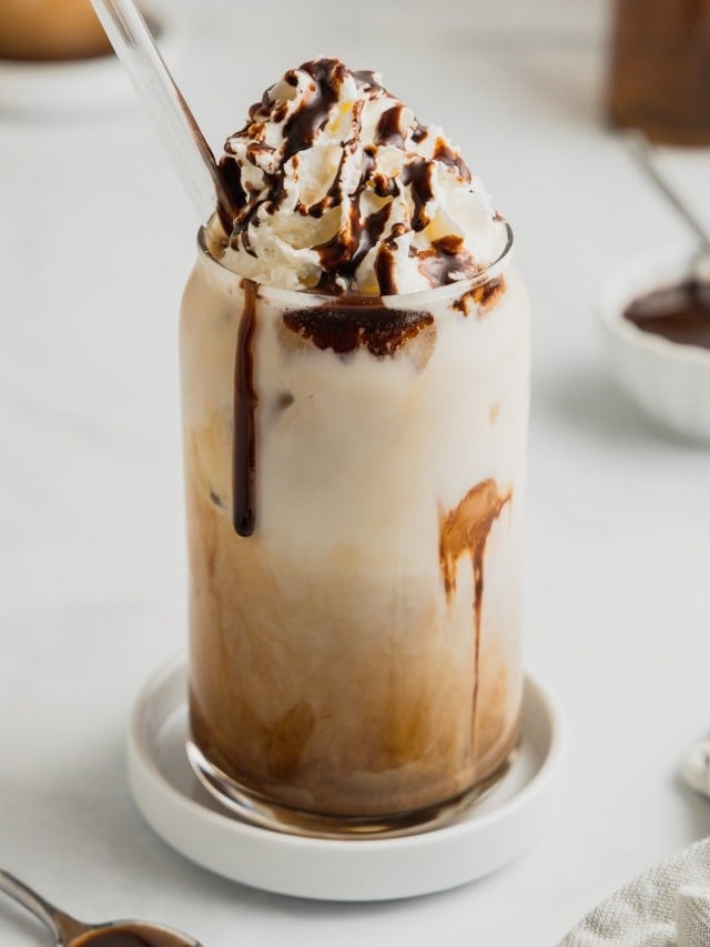 An Iced Mocha sits in a glass garnished with whipped cream and chocolate syrup.
