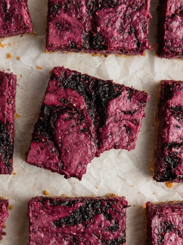 A piece of mulberry cheesecake with a bite taken out sits on a piece of parchment paper.