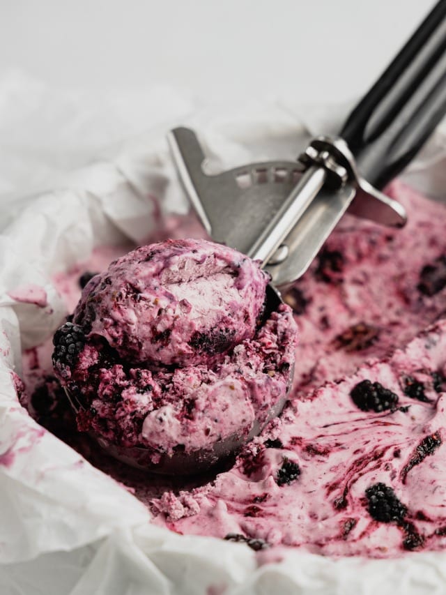An ice cream scoop filled with mulberry ice cream in a cake pan filled with frozen no-churn ice cream.