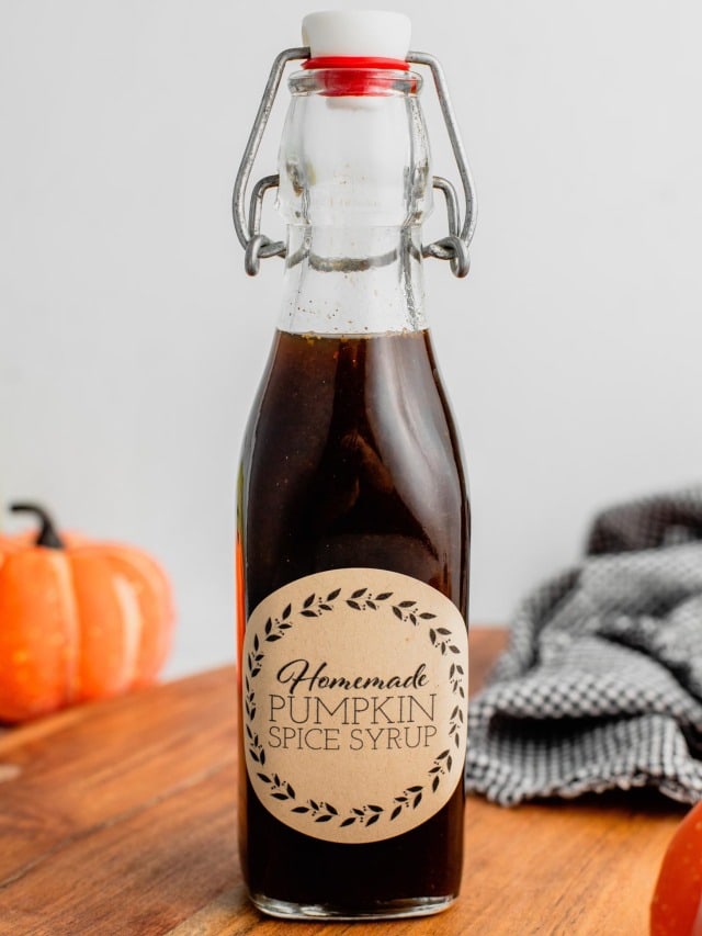 A glass jar filled with pumpkin spice syrup is labeled and sits on a wooden cutting board.