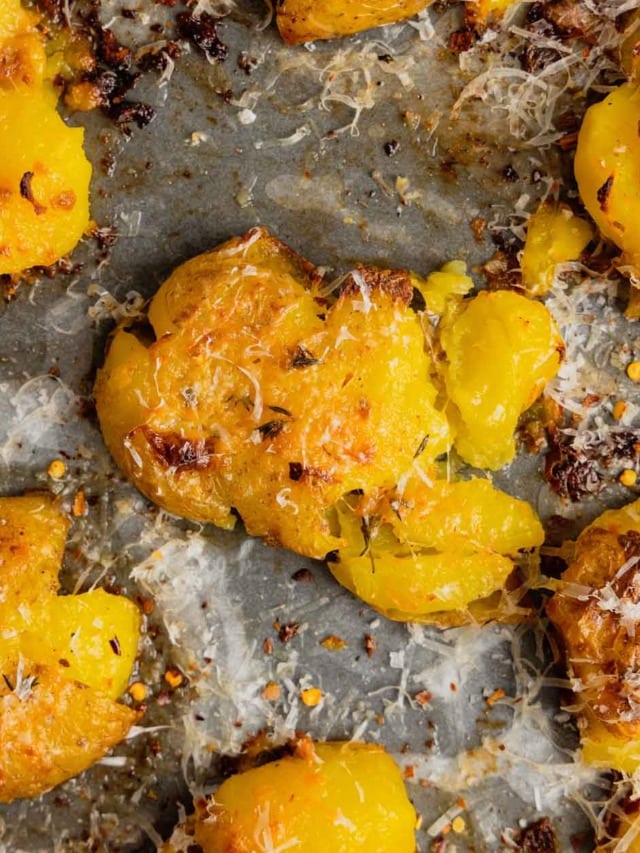 A close up of crispy smashed potatoes topped with shredded parmesan cheese on a rimmed baking sheet.