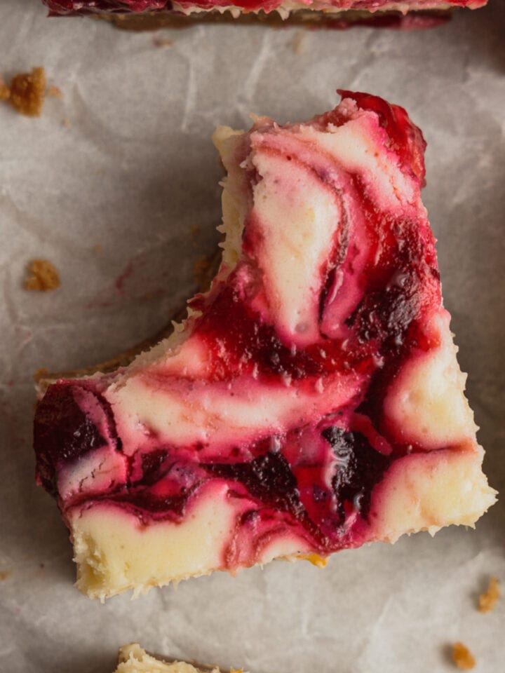 A cranberry cheesecake square with a bite taken out of it sits on a piece of parchment paper.