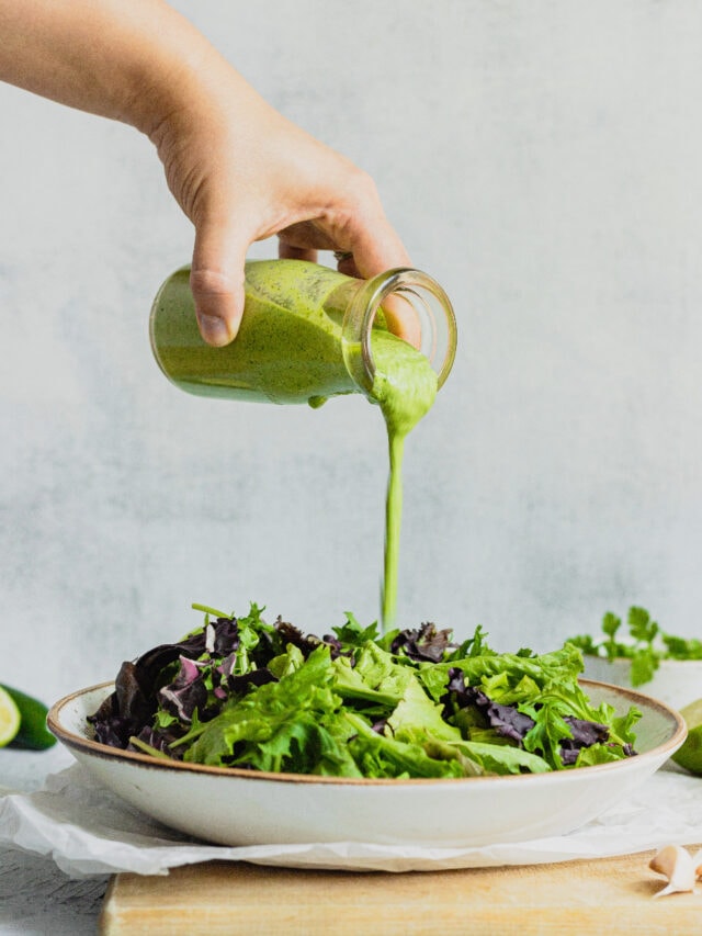 A hand pours green goddess salad dressing onto lettuce.