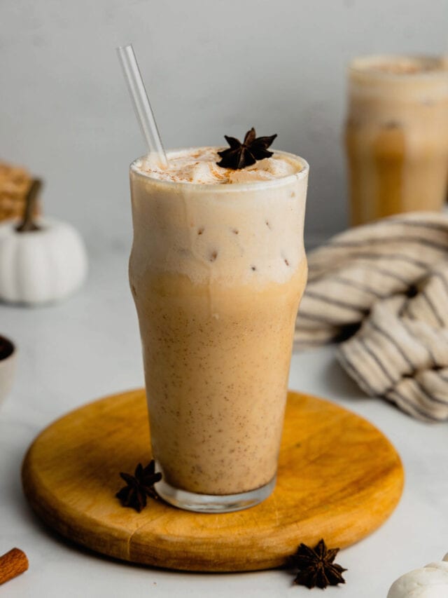 A tall glass filled with an iced chai latte topped with pumpkin cold foam and garnished with a straw, star anise, and pumpkin pie spice.