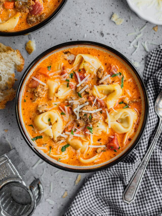 A bowl of sausage and tortellini soup is garnished with shaved parmesan.