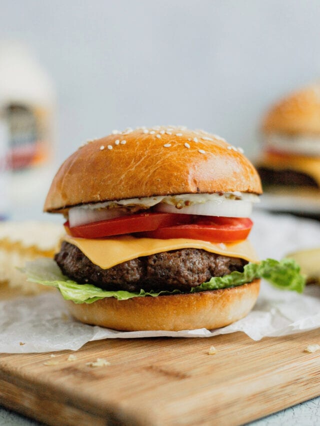 A ground venison burger sits on a cutting board with classic cheeseburger toppings.
