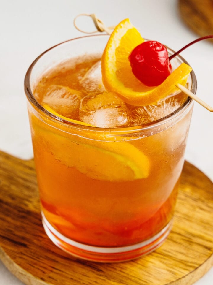 A brandy old fashioned sweet sits on a wooden serving board garnished with cherry and orange.