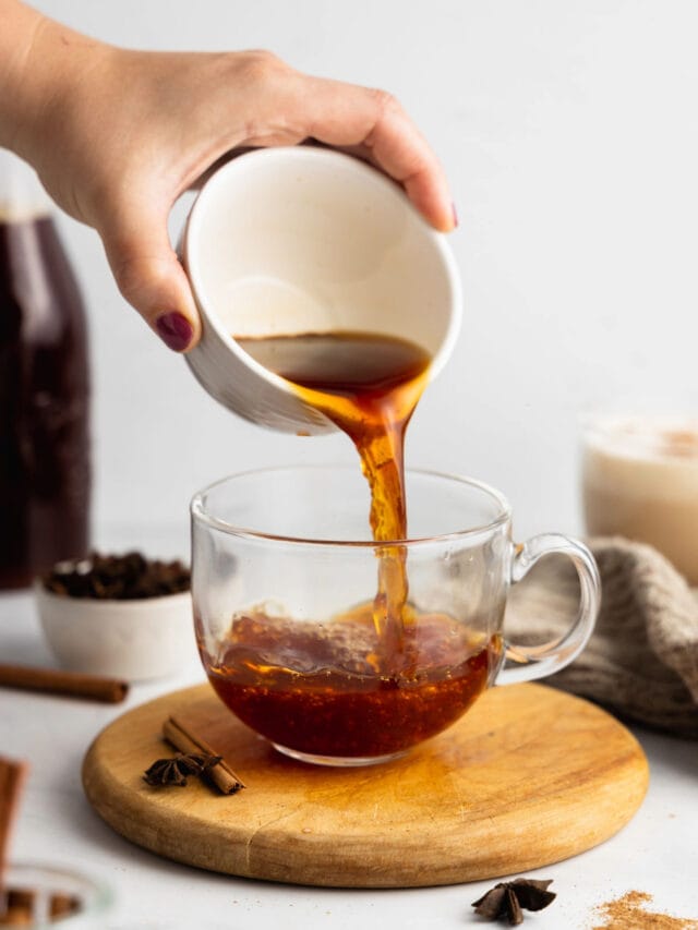 A hand pours chai tea latte concentrate into a mug.