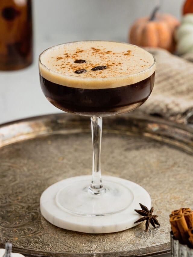 A pumpkin spice espresso martini sits on a marble coaster on a silver tray.