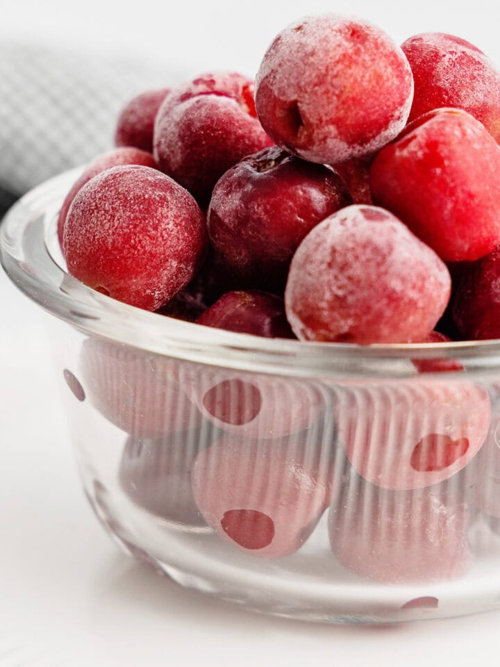 A small glass bowl filled with frozen, pitted cherries.