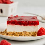 A slice of raspberry pretzel jello salad sits on a white plate garnished with fresh raspberries.