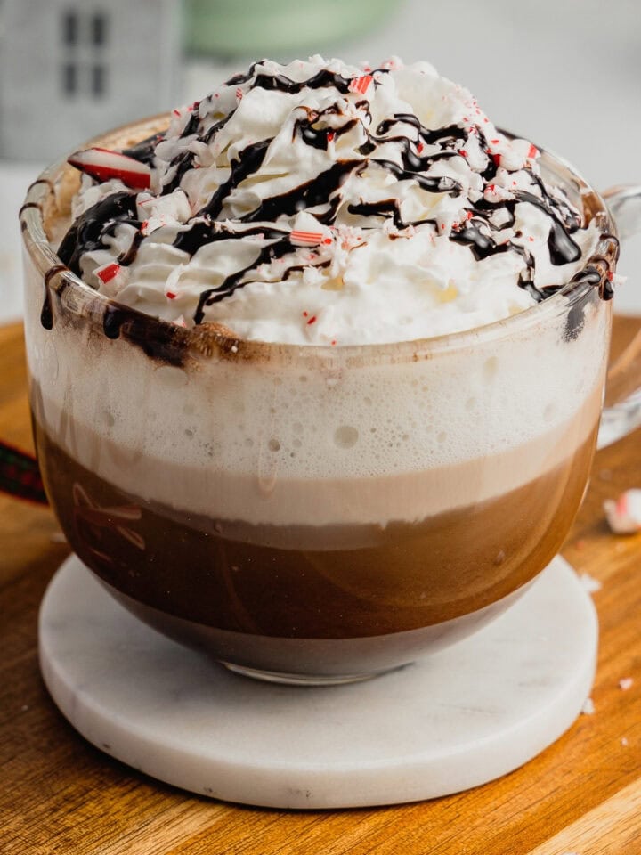 A large glass mug is filled with a peppermint mocha that is garnished with chocolate syrup and crushed candy canes.