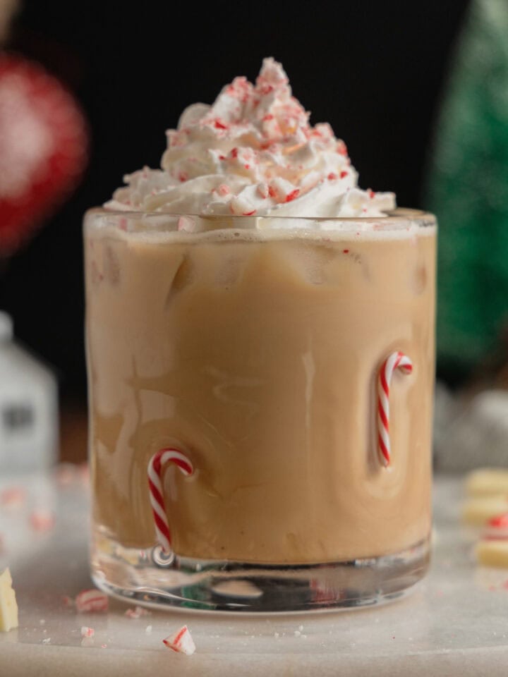 A glass with candy cane embellishments filled with a peppermint white chocolate mocha and garnished with whipped cream and crushed peppermint candies.