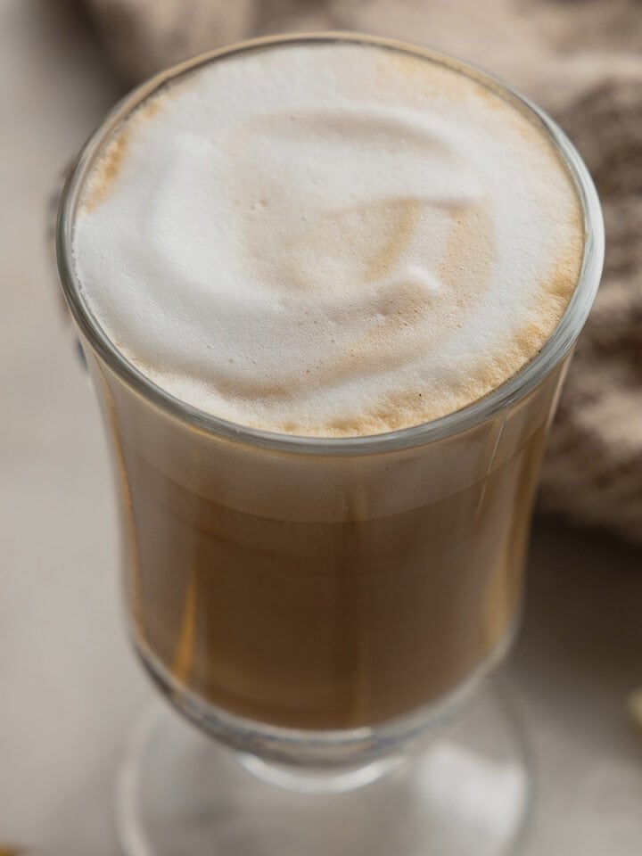 A glass mug filled with a white mocha latte on a white marble serving board.
