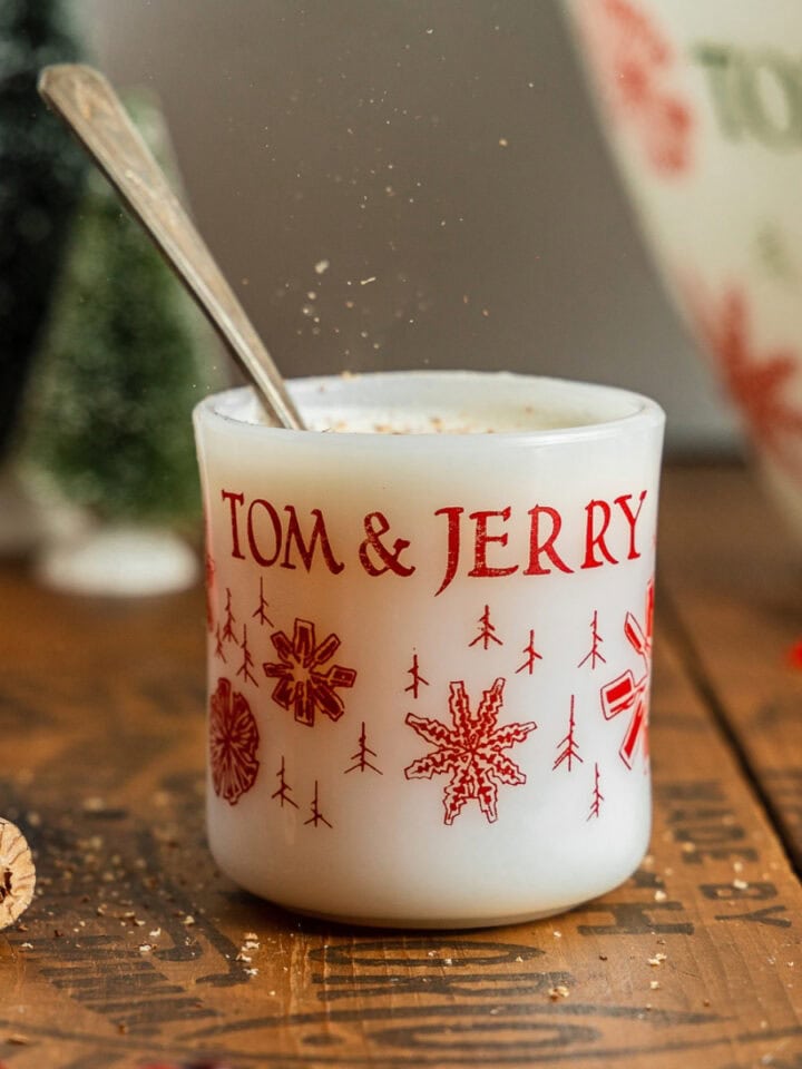 A mug filled with tom and jerry batter is sprinkled with nutmeg.