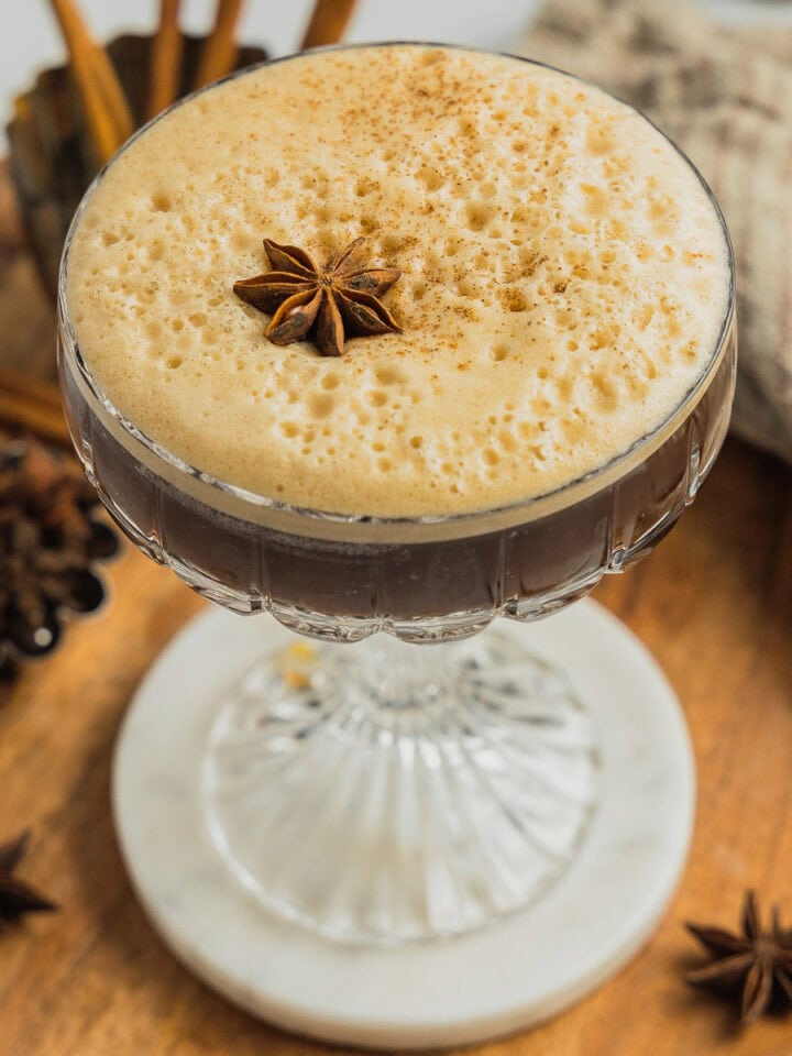 A fluted coupe glass filled with a dirty chai espresso martini that's got a foamy top and is garnished with a star anise.