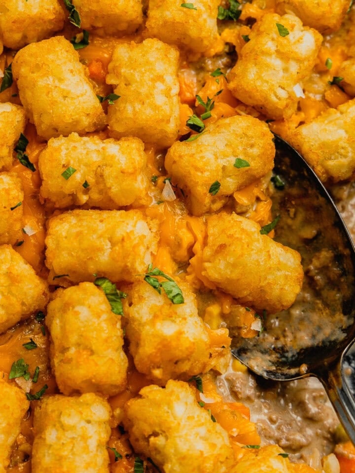 A spoon sits in a partially scooped out pan of venison tater tot casserole.