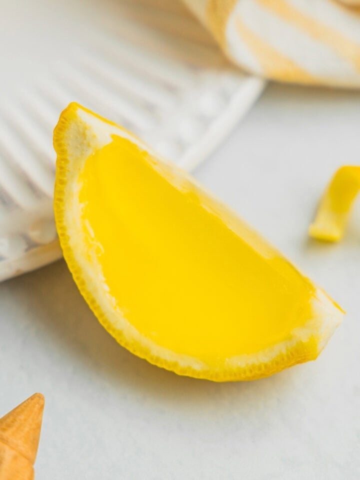 A lemon drop jello shot in a lemon rind wedge sits on a backdrop.