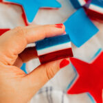 A woman's hand with red painted nails holds a red, white, and blue layered jello shot.
