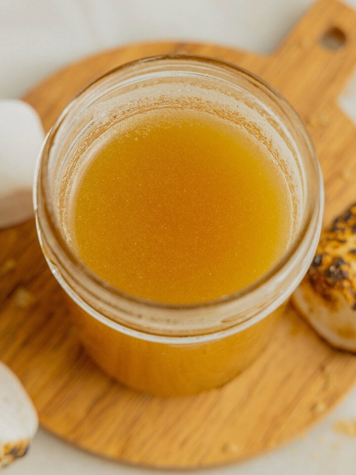A small glass jar filled with toasted marshmallow coffee simple syrup on a wooden board surrounded by toasted marshmallows.