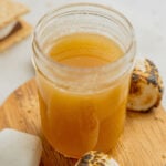 A small glass jar filled with toasted marshmallow syrup on a wooden board surrounded by toasted marshmallows.