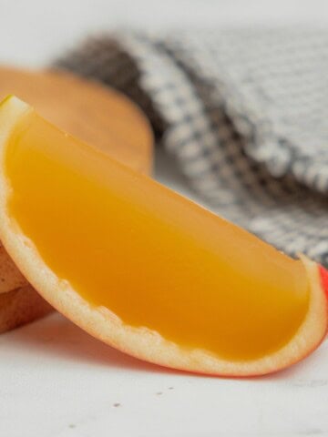 A cored apple slice filled with an apple cider jello shot rests on a small wooden board.